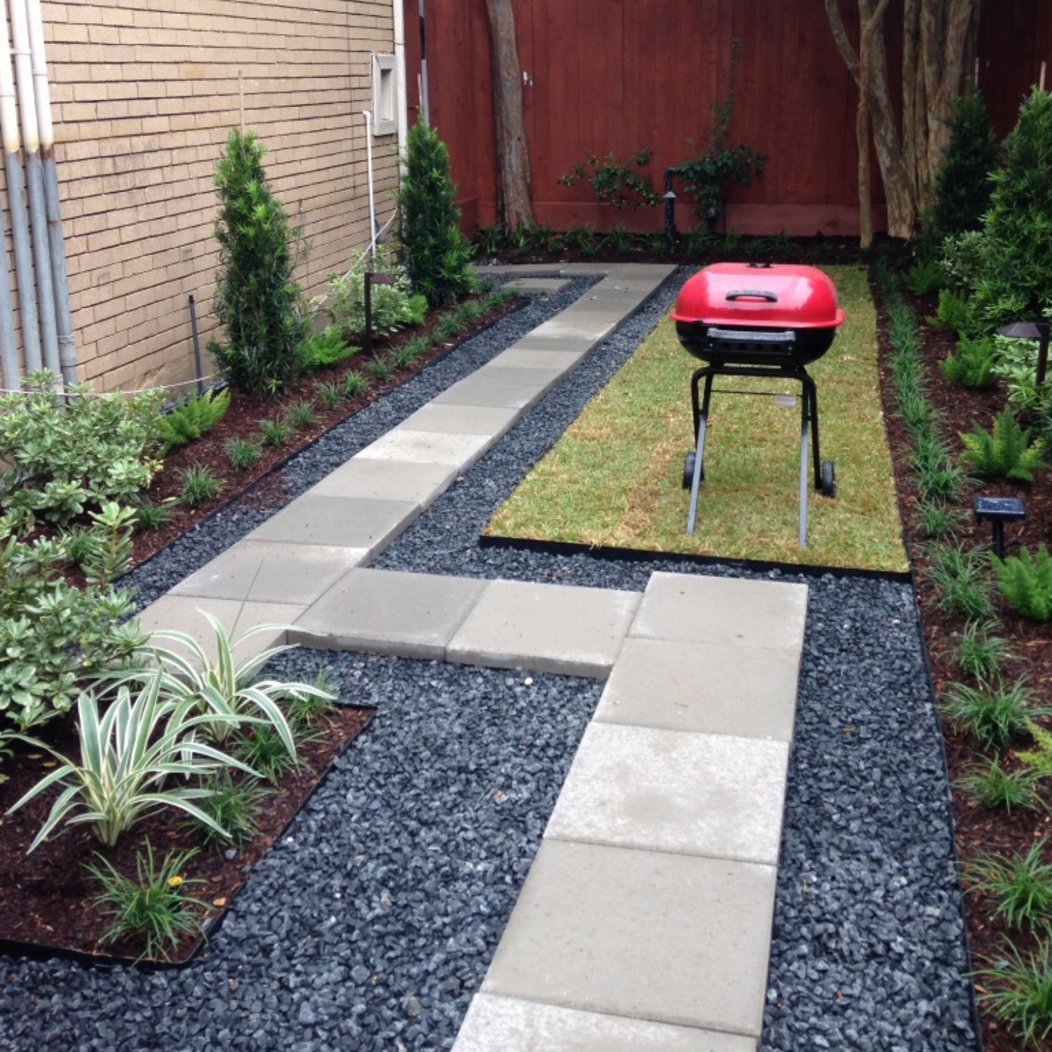 Front Yard Landscape with a beautiful flower bed, various greenery and shrubs. Potted spiral juniper with flowers and trailing vines.